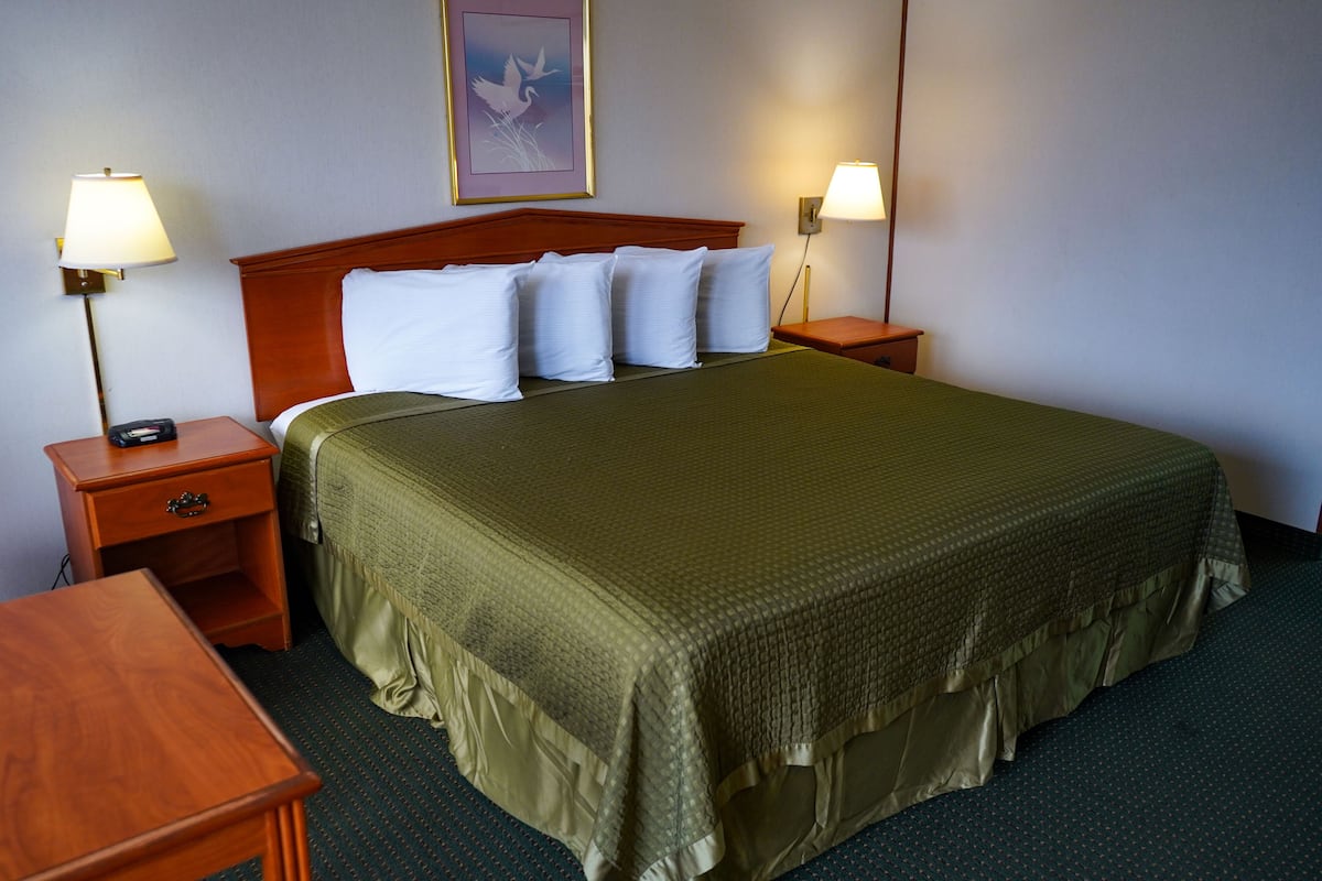 Une chambre d’hôtel avec un grand lit, deux tables de chevet, une petite table, une lampe fixée au mur et un tableau encadré accroché au mur.