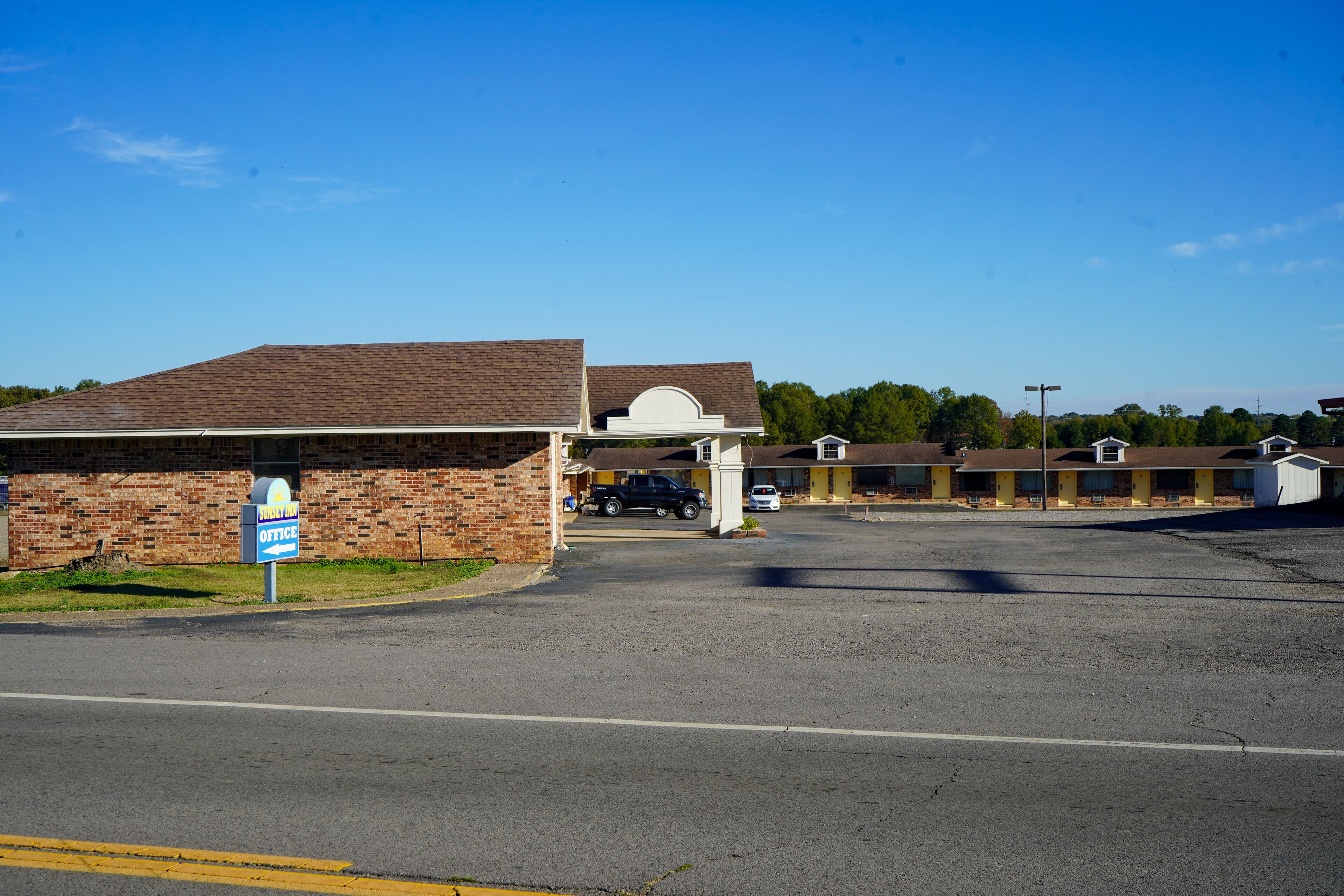 A motel with a brick facade, a covered parking area, and a row of motel units with yellow doors.