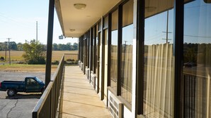 A covered balcony with large windows overlooking a parking area.
