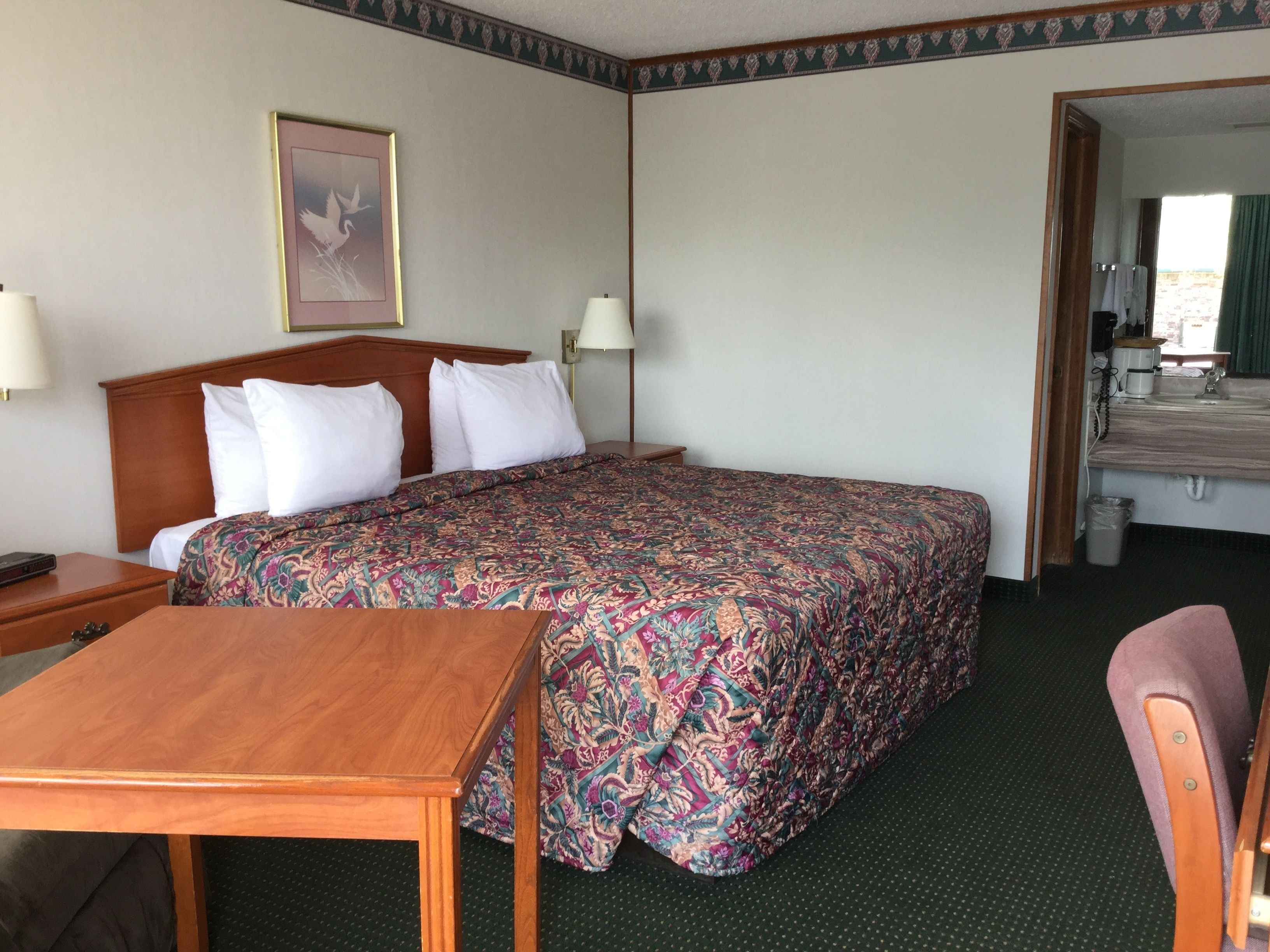 A hotel room with a large bed, a wooden nightstand, a table, and a chair.