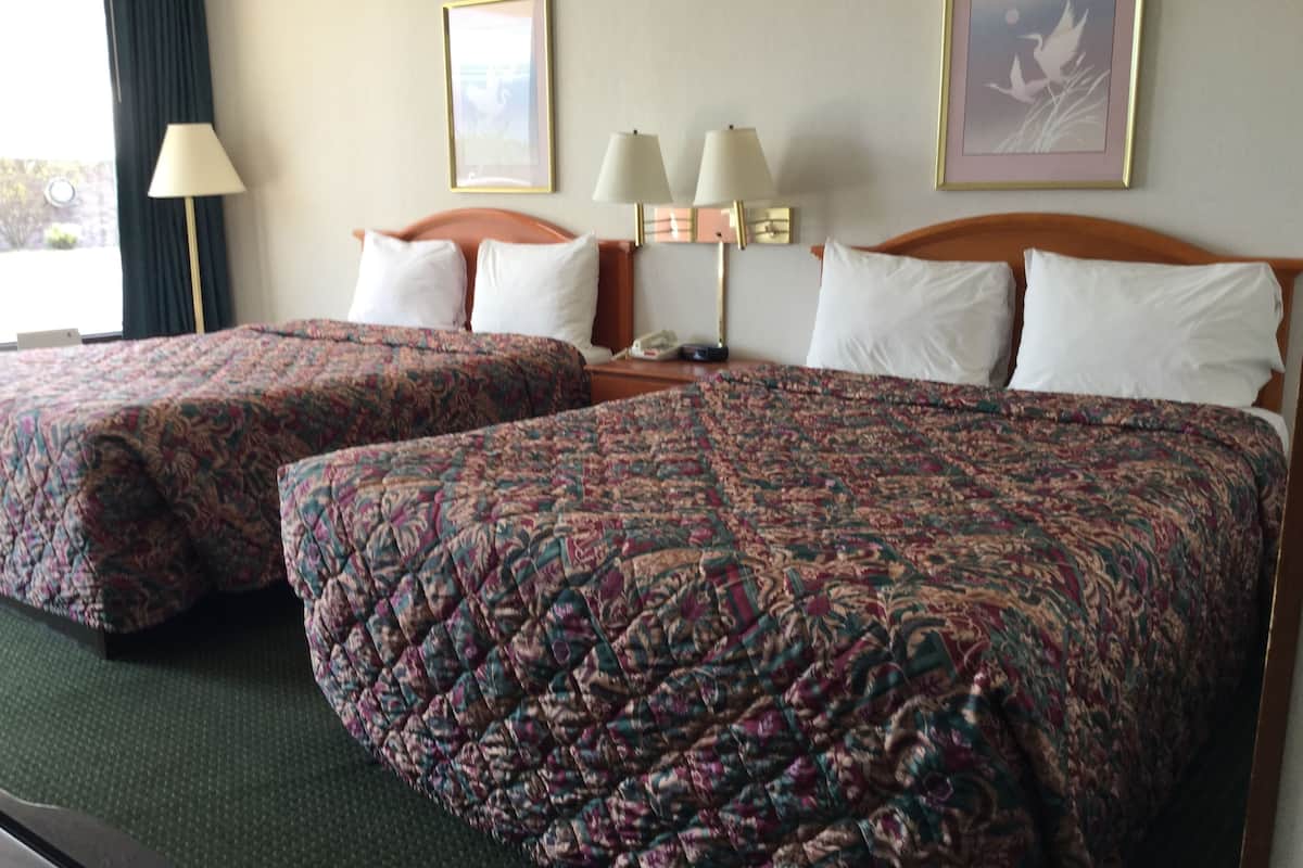 Une chambre d’hôtel avec deux lits, chacun recouvert d’une couvre-lit à motifs floraux, une table de chevet avec une lampe et des œuvres d’art encadrées accrochées au mur.