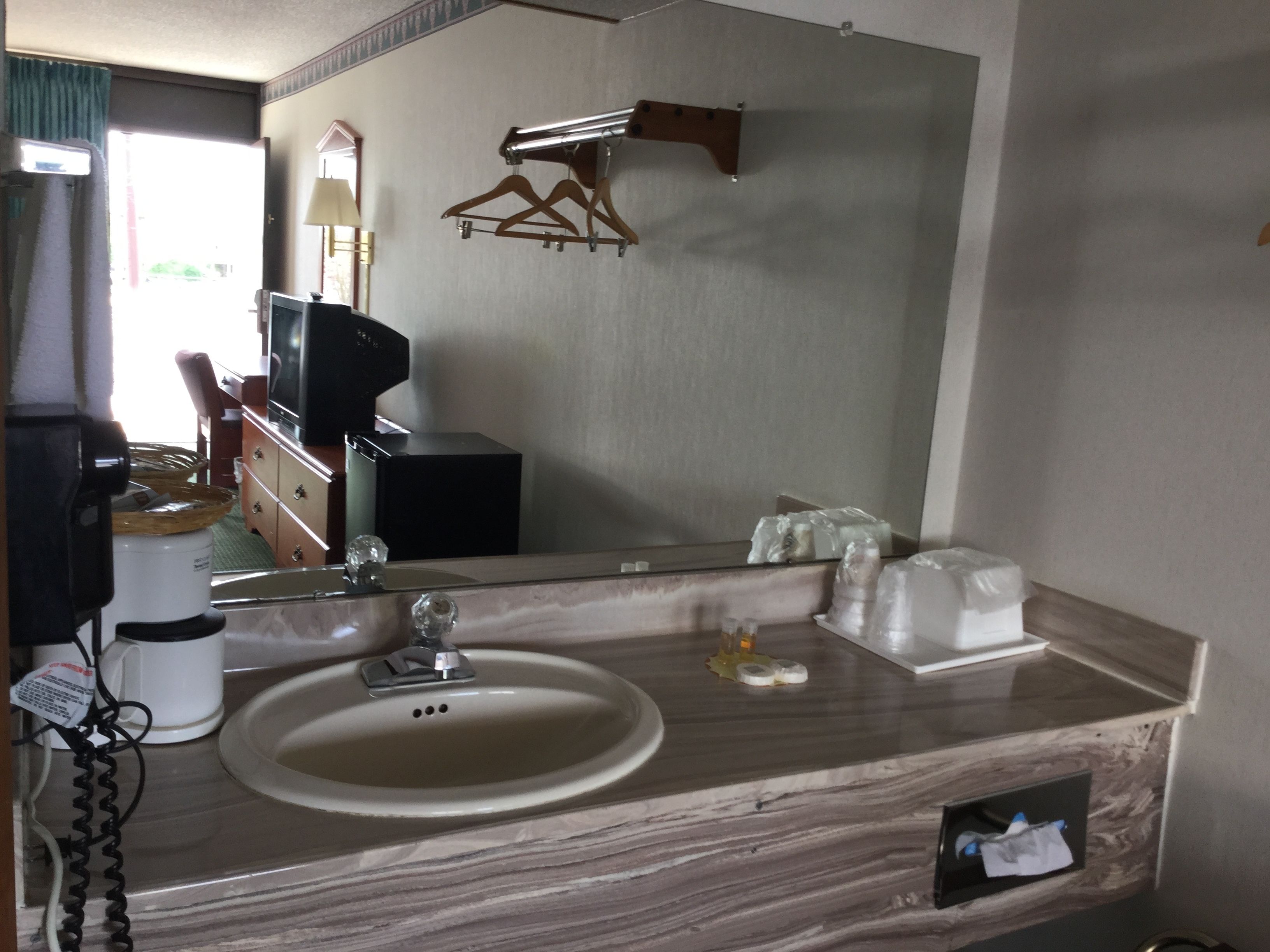 Une salle de bain d’hôtel avec un lavabo, un miroir et un porte-manteau en bois.