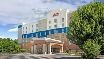 Ein Hampton Inn & Suites Hotel mit zentralem Eingang, mehreren Etagen und einem Parkplatz.