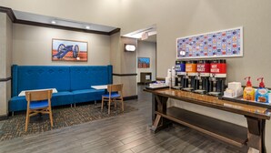 A hotel lobby with a blue sofa, two chairs, a coffee station with multiple drink dispensers, and a wall with a colorful pattern. - Hampton Inn & Suites Fort Mill (Fort Mill)