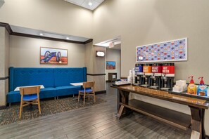A hotel lobby with a blue sofa, two chairs, a coffee station with multiple drink dispensers, and a wall with a colorful pattern. - Hampton Inn & Suites Fort Mill (Fort Mill)
