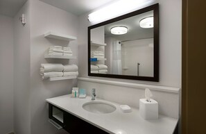Un baño moderno con un espejo grande, repisas blancas con toallas, un lavamanos y una zona de ducha.