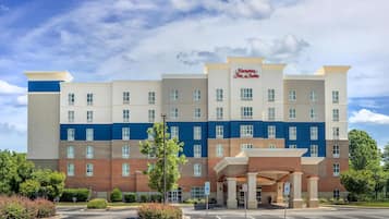Ein mehrstöckiges Hotel mit einem gut sichtbaren Hampton Inn & Suites Schild, einem Parkplatz und einem begrünten Eingangsbereich.