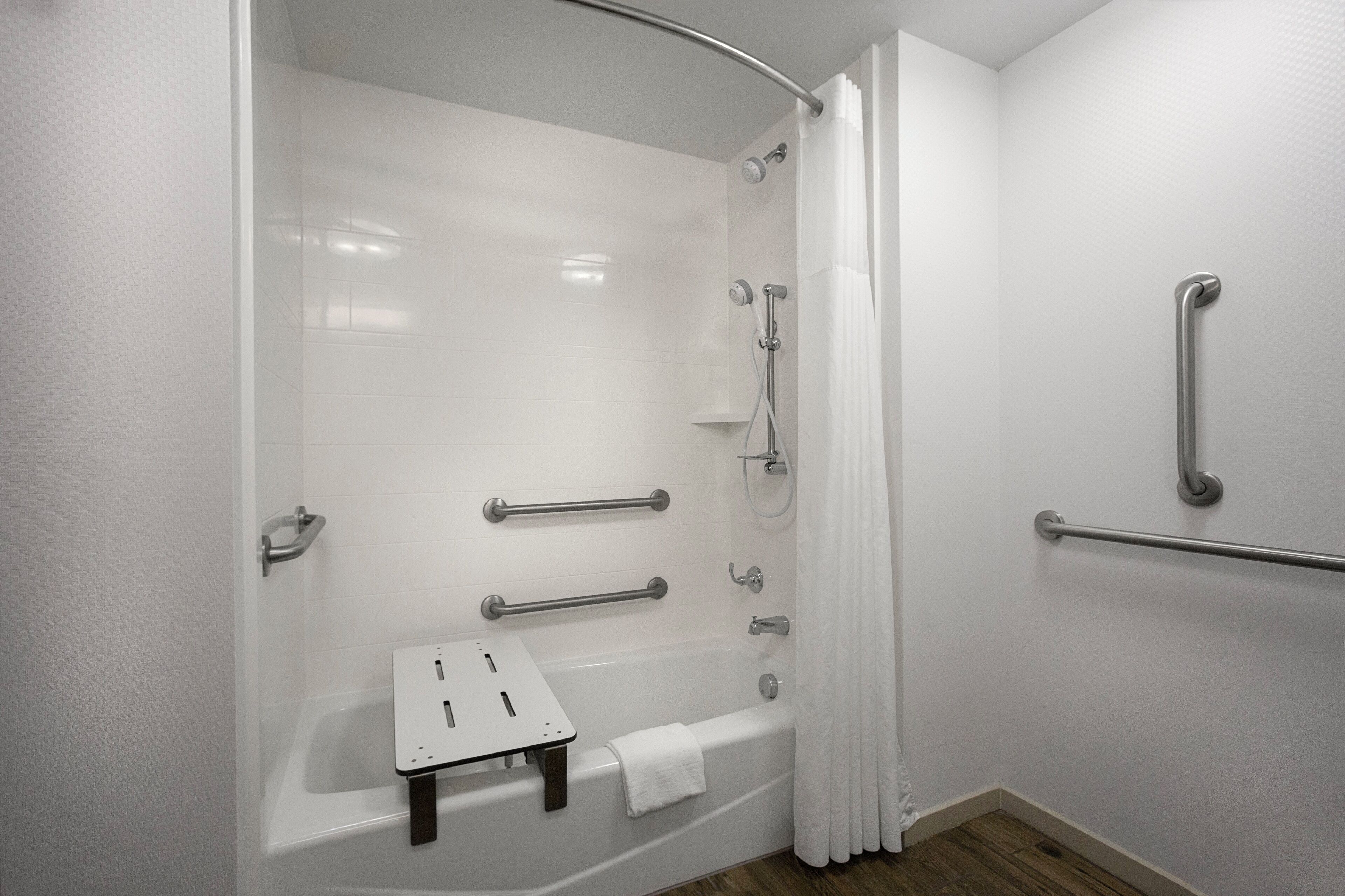 Un bagno moderno con doccia a filo pavimento, maniglie di sostegno, una piccola panca e un porta asciugamani.