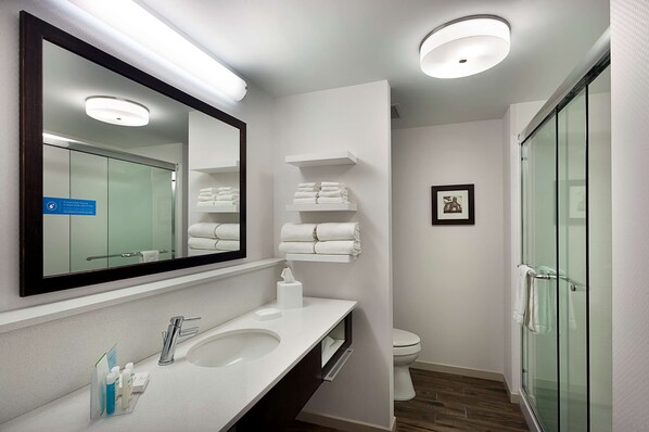 Un baño moderno con un espejo grande, sanitarios blancos, cabina de ducha con mampara de cristal y toallas ordenadas.