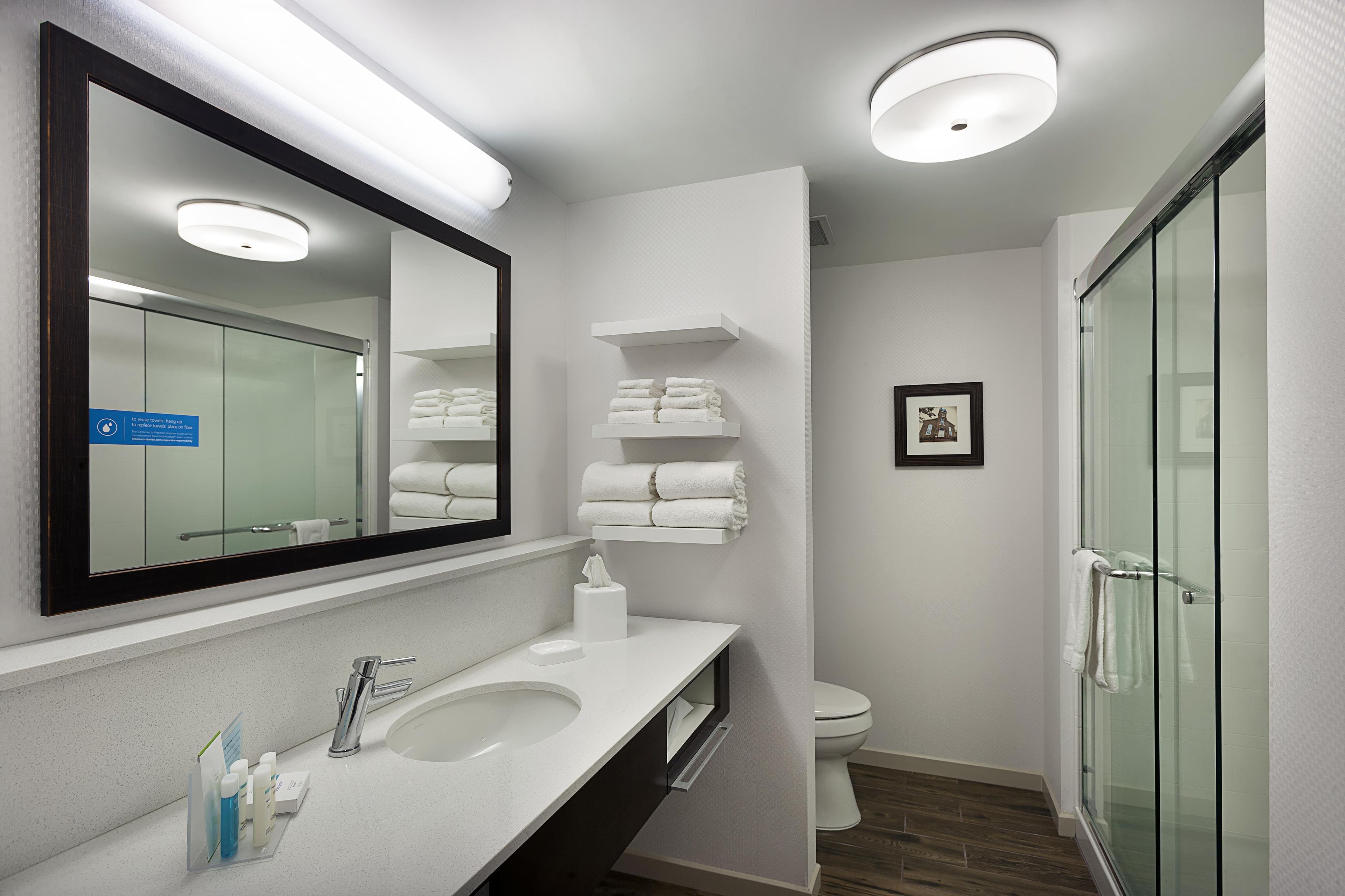 A modern bathroom with a large mirror, a sink, a toilet, and a glass shower enclosure.