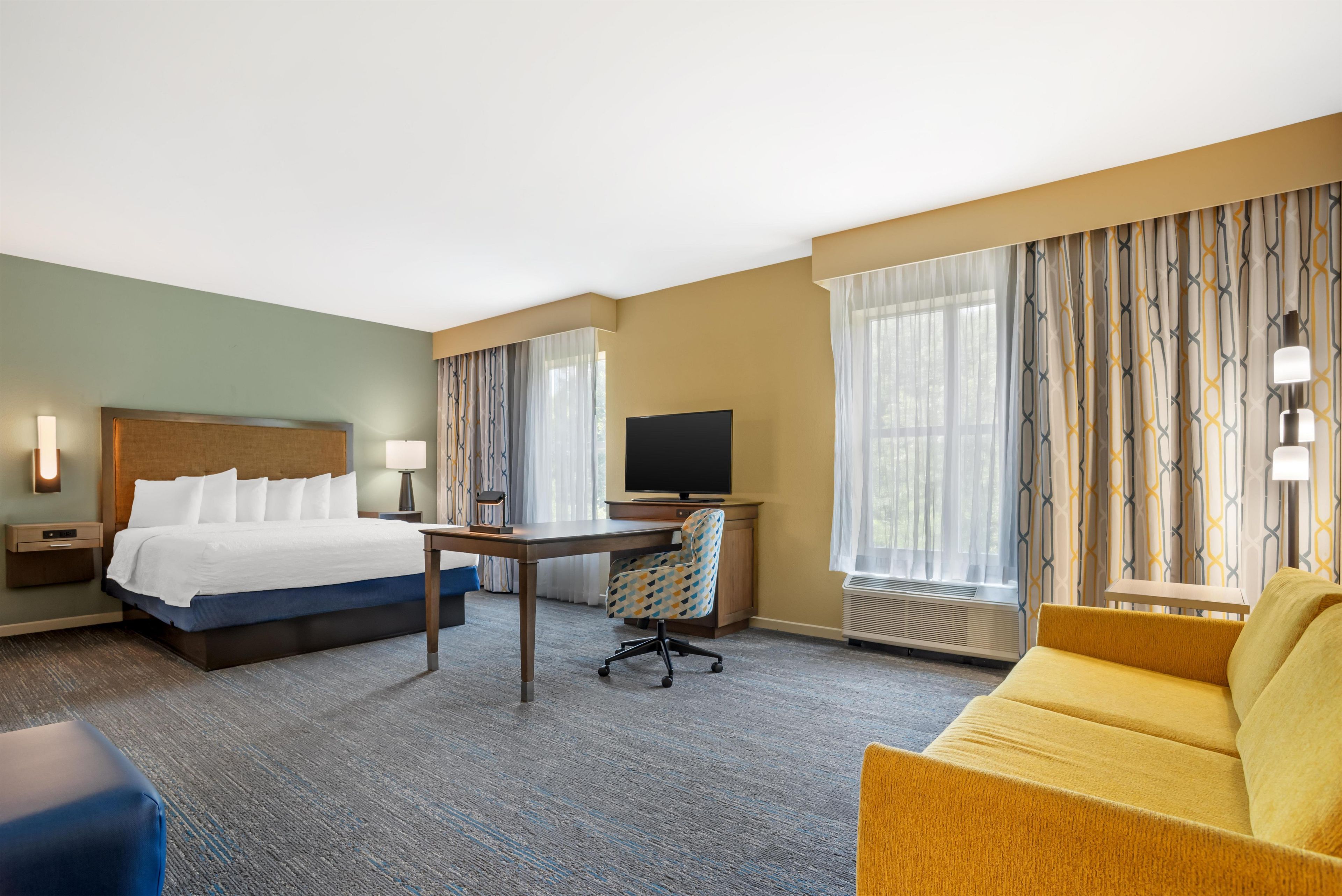 Une chambre d’hôtel avec un lit, un bureau, une télévision et un canapé.