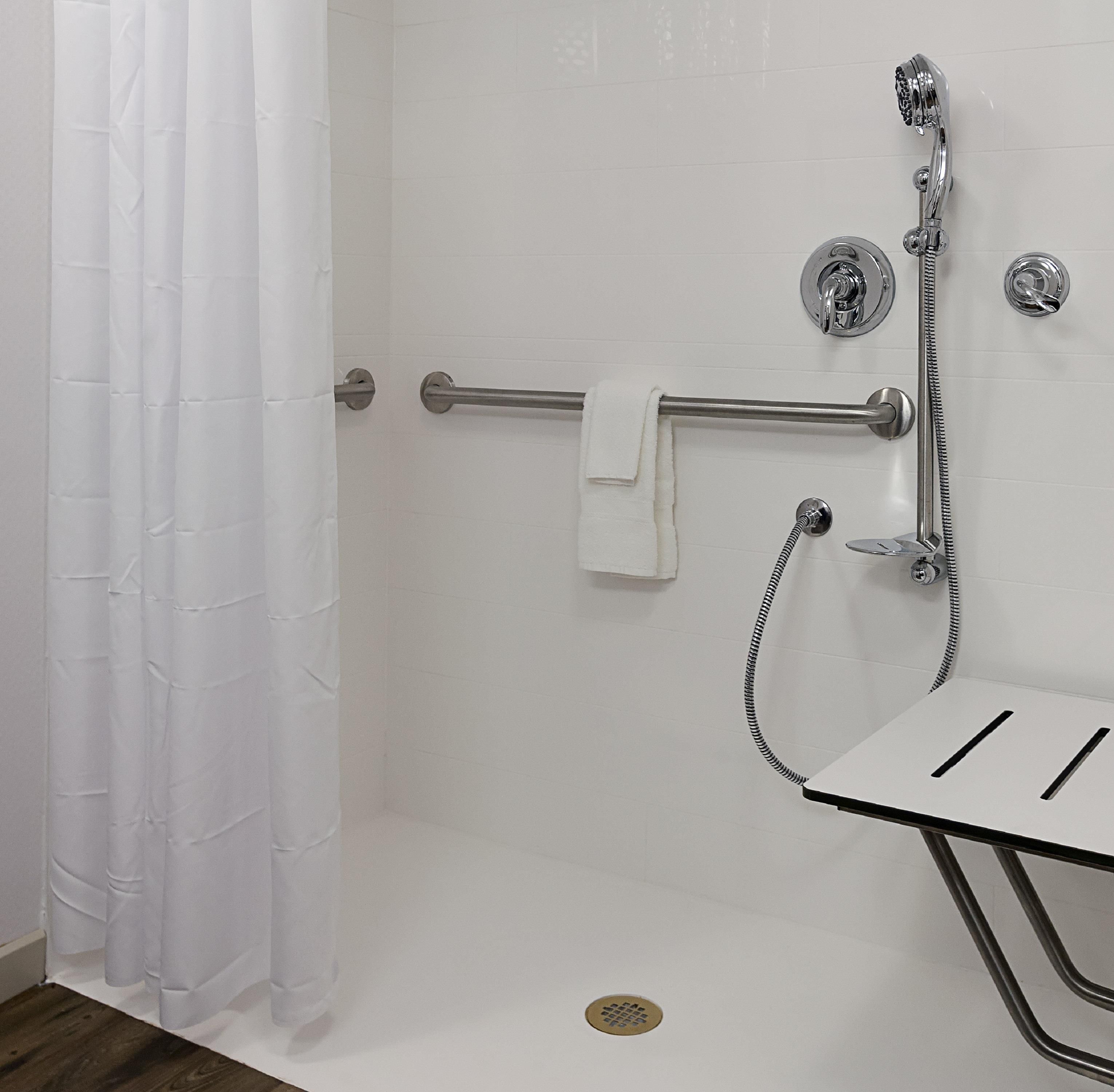 A shower area with a grab bar, a handheld showerhead, and a towel rack.