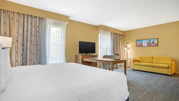 Habitación de hotel con una cama grande, un escritorio con televisor, un sofá y un cuadro en la pared.