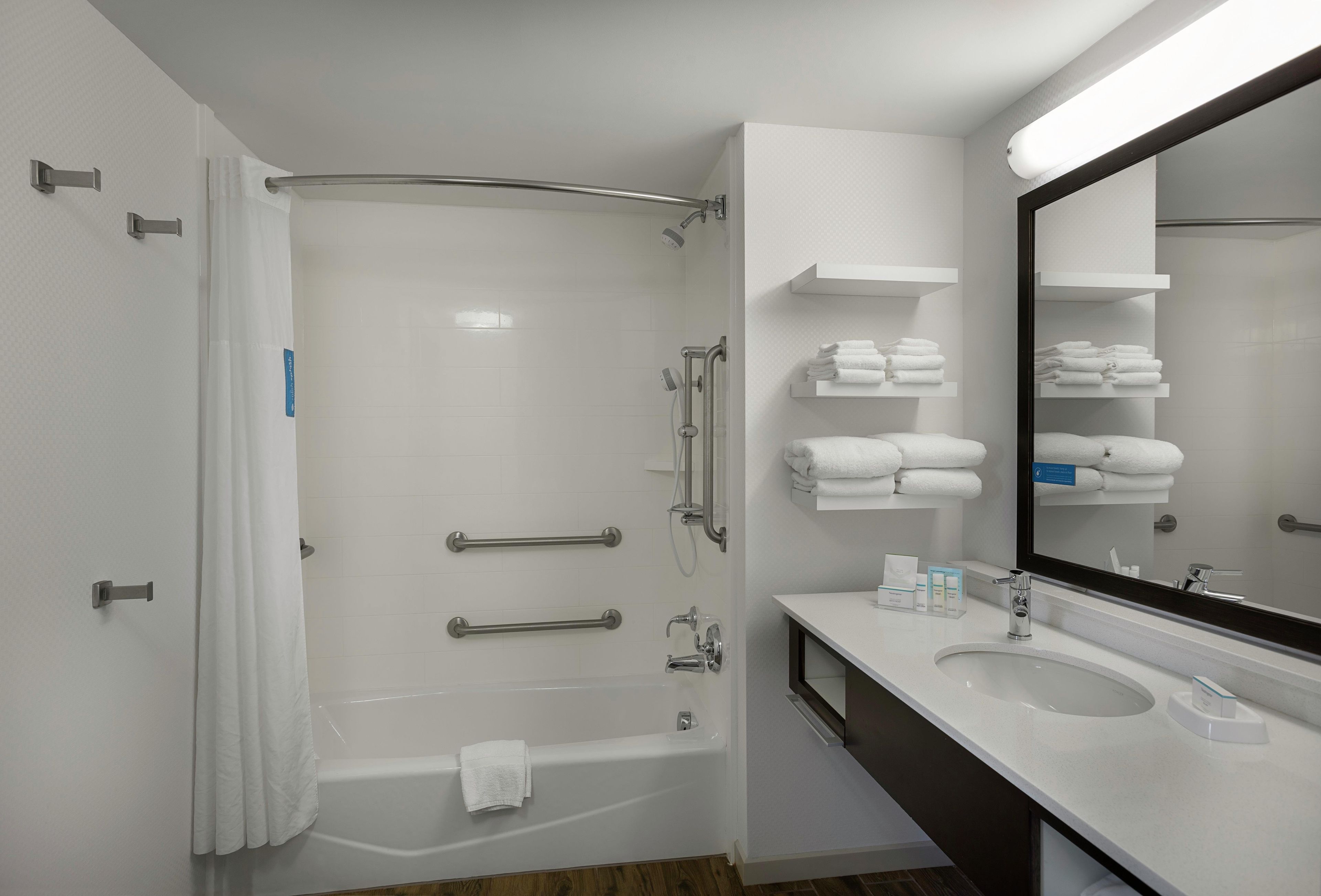 Un baño moderno con bañera, ducha con puerta de cristal, tocador con espejo y perchero para toallas.