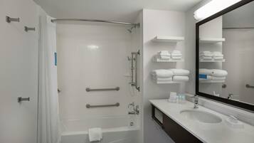 Un baño moderno con bañera, ducha con puerta de cristal, tocador con espejo y perchero para toallas.