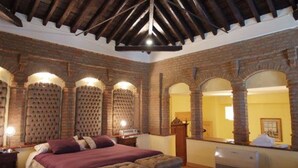 A room with a high ceiling, exposed wooden beams, brick walls, and a bed with a headboard. - Hotel Palacio de Oñate Spa (Guadix)