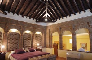 A room with a high ceiling, exposed wooden beams, brick walls, and a bed with a headboard. - Hotel Palacio de Oñate Spa (Guadix)