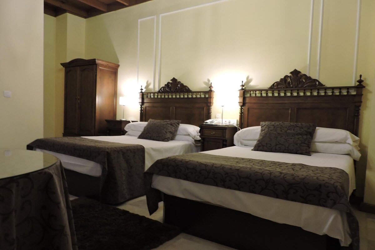 A hotel room with two single beds, a wooden wardrobe, a round table, and a small rug.