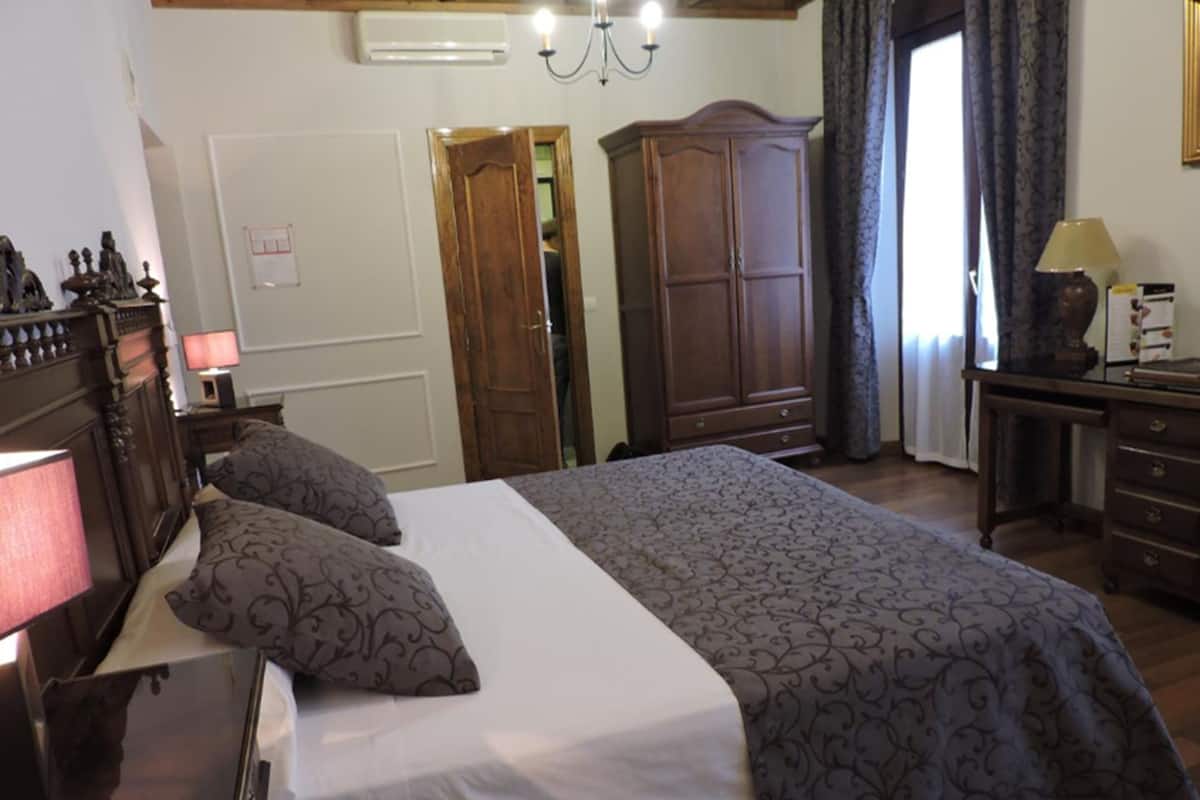 A bedroom with a large bed, a wardrobe, a desk with a lamp, and a mirror.