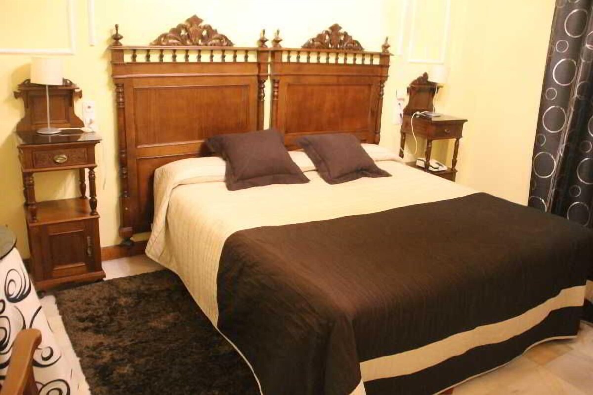 Ein Schlafzimmer mit einem hölzernen Bett, zwei Nachttischen, einem Beistelltisch und einer schwarz-weiß gestreiften Bettdecke.