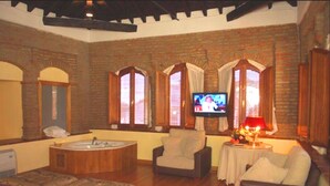 A room with a wooden bathtub, a television, and a cozy seating area with a table and lamp. - Hotel Palacio de Oñate Spa (Guadix)