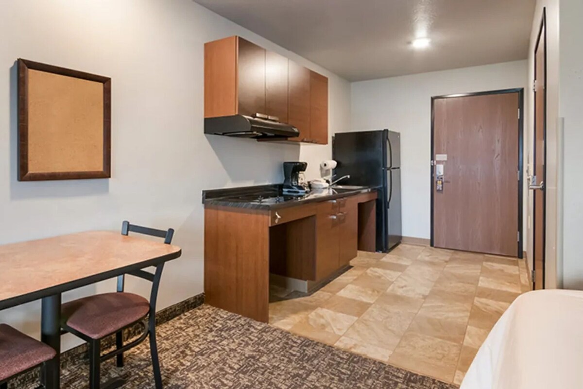 Cocina compacta con una mesa de madera, sillas, refrigerador y cafetera.