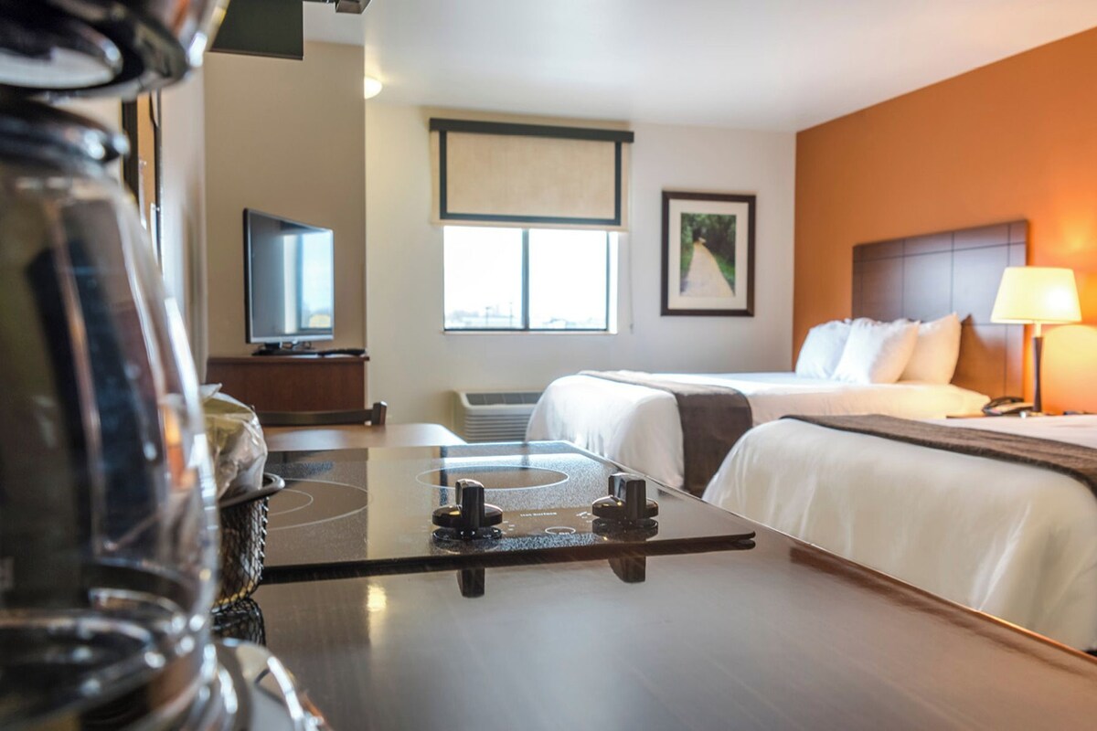 Habitación de hotel con dos camas, un escritorio, una silla, un televisor y una ventana.