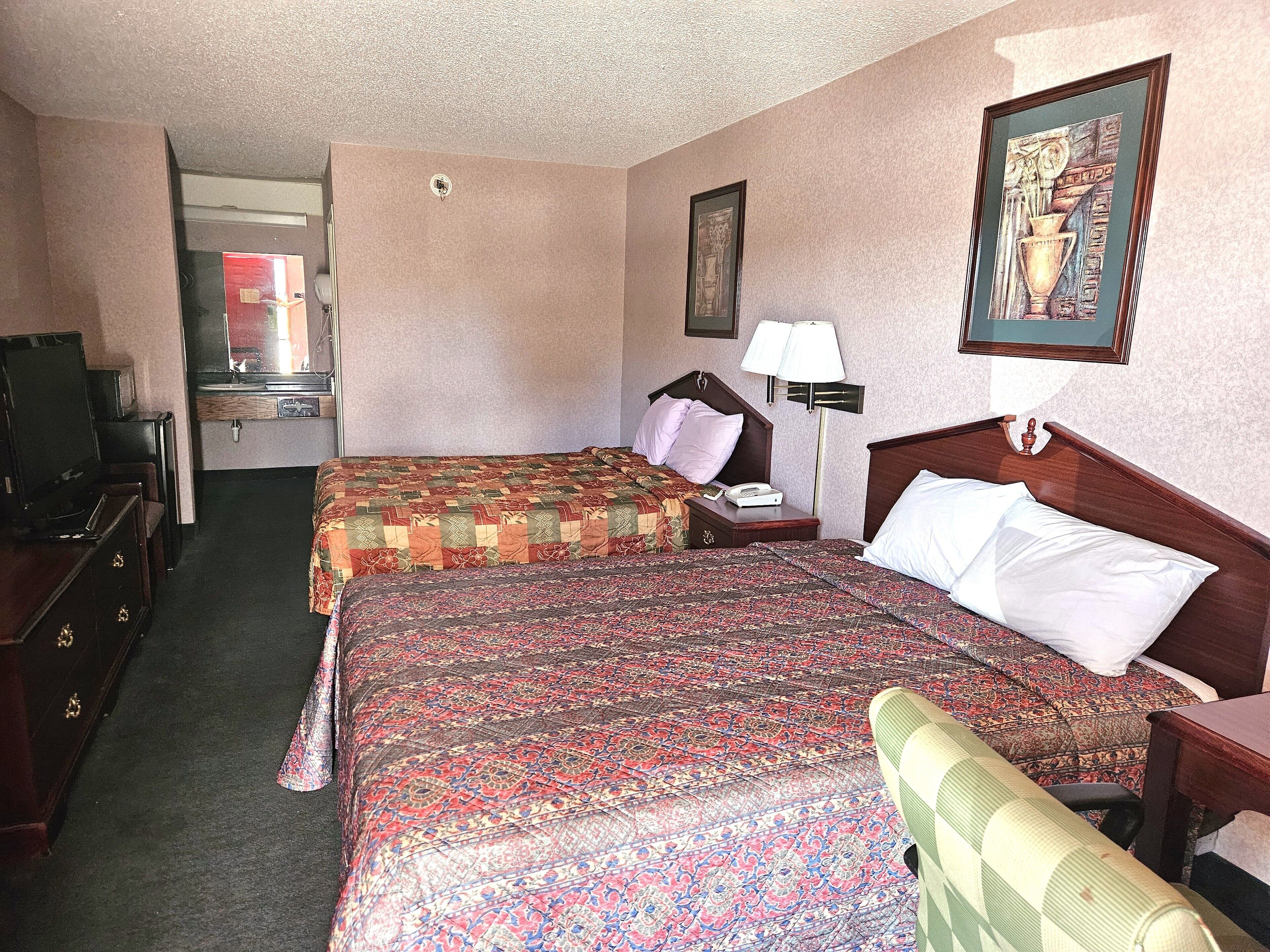 A hotel room with two beds, a TV, a desk, and a lamp.