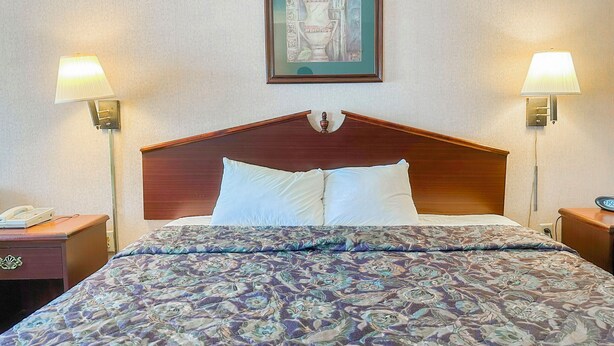 A hotel room with a wooden headboard, two bedside lamps, a telephone, and a framed artwork above the bed.