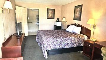 A hotel room with a bed, bedside tables, a desk, a chair, a lamp, a telephone, and a television.