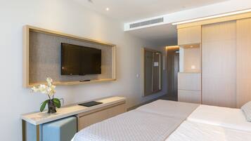 Una habitación de hotel moderna con una cama grande, un televisor de pantalla plana montado en la pared, un pequeño escritorio con una silla y un vestidor.