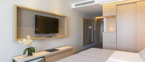 Ein modernes Hotelzimmer mit einem großen Bett, einem Flachbildfernseher an der Wand, einem kleinen Schreibtisch mit Stuhl und einem begehbaren Kleiderschrank.