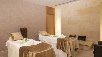 Habitación de hotel con dos camas, cada una cubierta con un edredón marrón, un banco de madera y una mesita de noche con artículos de tocador.