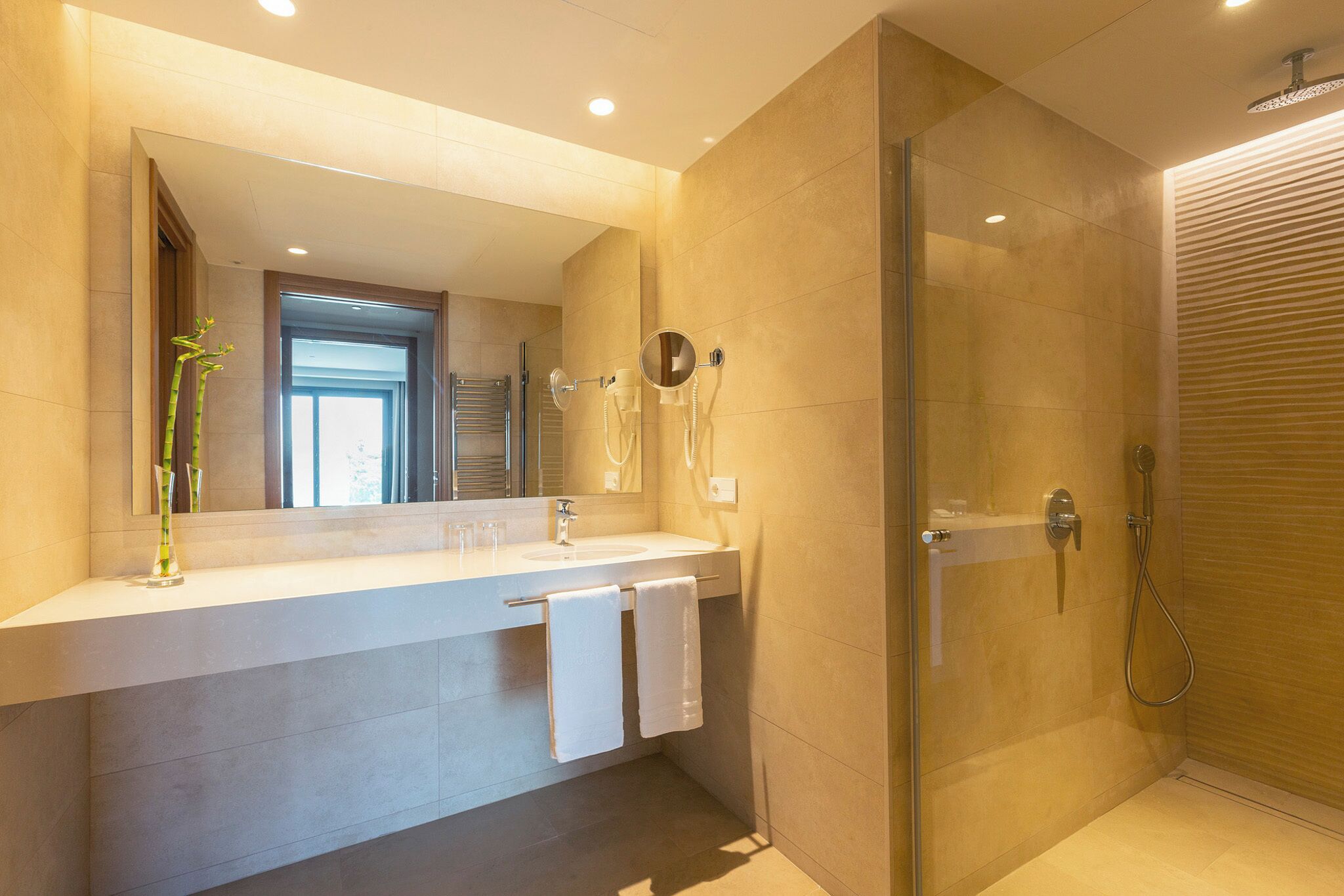 Un baño moderno con ducha de vidrio, un espejo grande y un tocador doble.