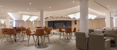 A modern conference room with a stage, multiple seating areas, and a carpeted floor.
