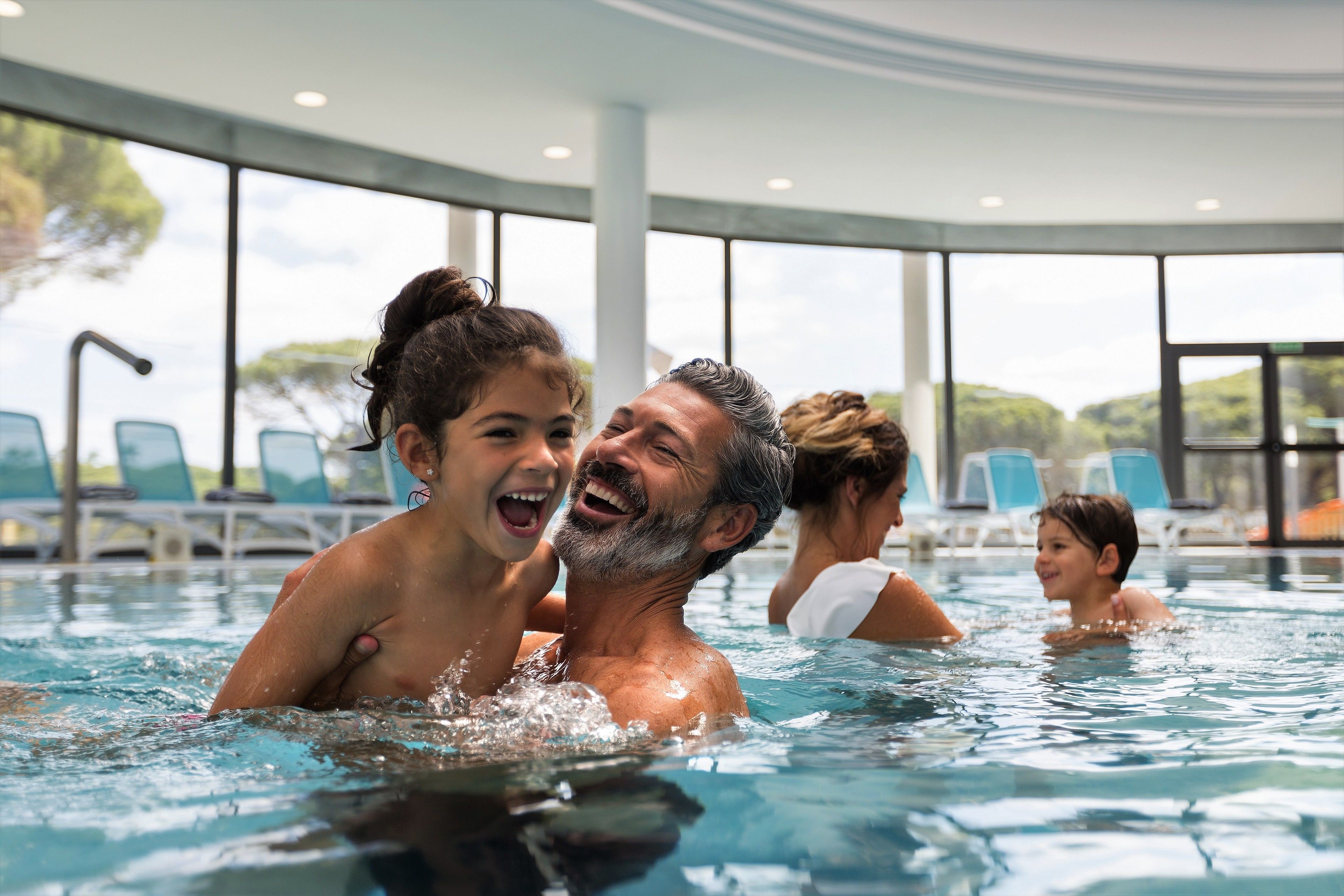Zona de piscina con agua cristalina, sillas de descanso y grandes ventanales.
