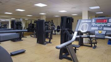 Uma academia com diversos equipamentos de ginástica, incluindo esteira, aparelhos de musculação e um banco.