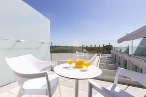 A modern outdoor seating area with white chairs and a table, featuring a glass partition and a clear view of the landscape. - Hipotels Barrosa Park (Chiclana de la Frontera)