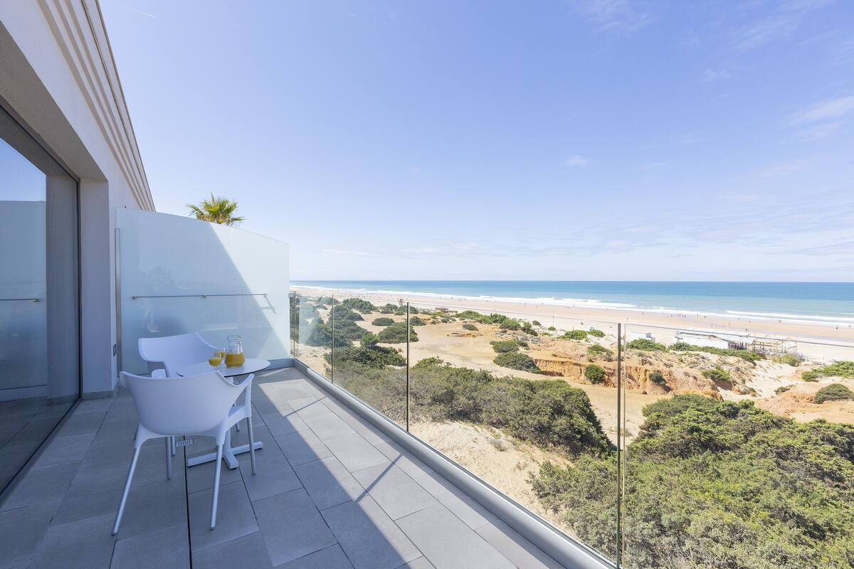 A balcony with a glass railing overlooking a beach and ocean.