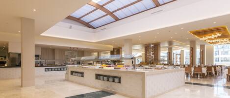 A spacious hotel lobby with a high ceiling, a central island with a buffet, and a large skylight.