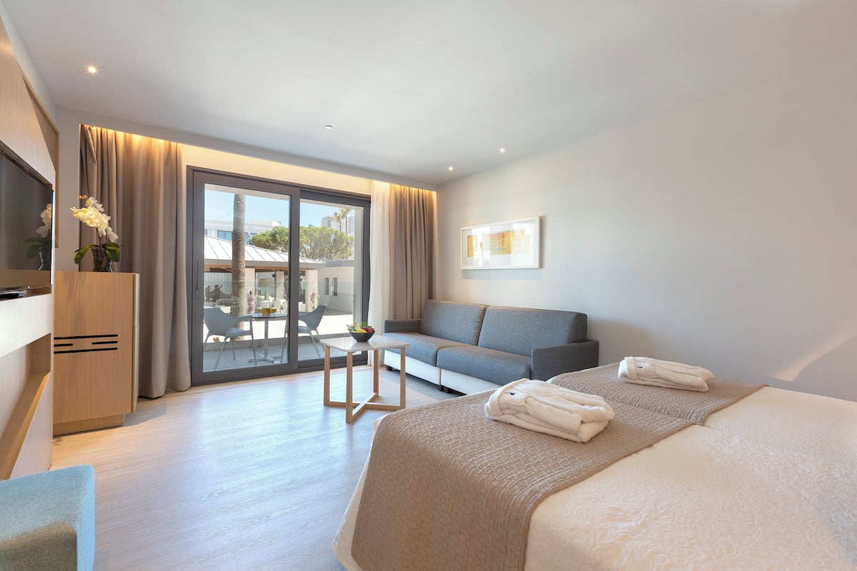 Quarto de hotel moderno com uma cama grande, um sofá, uma mesa pequena e vista para o exterior.