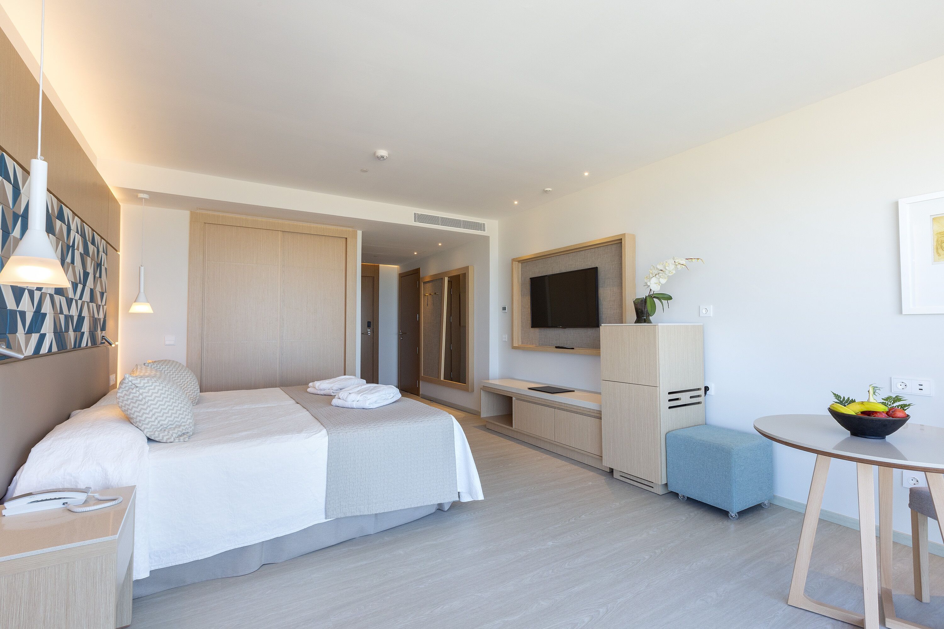Habitación de hotel moderna con cama, mesita de noche, televisión y un pequeño comedor.