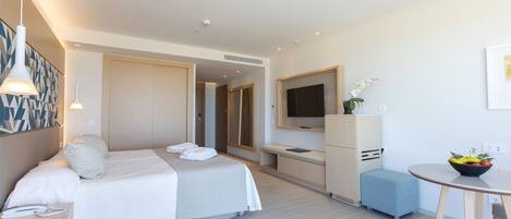 Habitación de hotel moderna con cama, mesita de noche, televisión y un pequeño comedor.