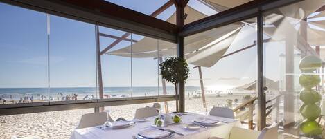 Un comedor con vista a la playa, manteles blancos y sillas acolchadas de color verde.