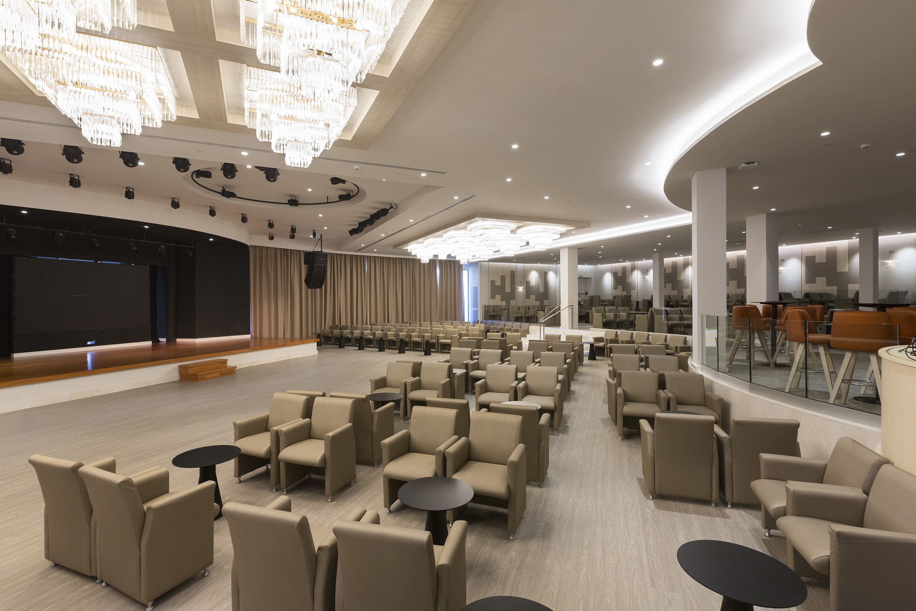 A spacious conference room with rows of chairs, a stage, and a large screen.