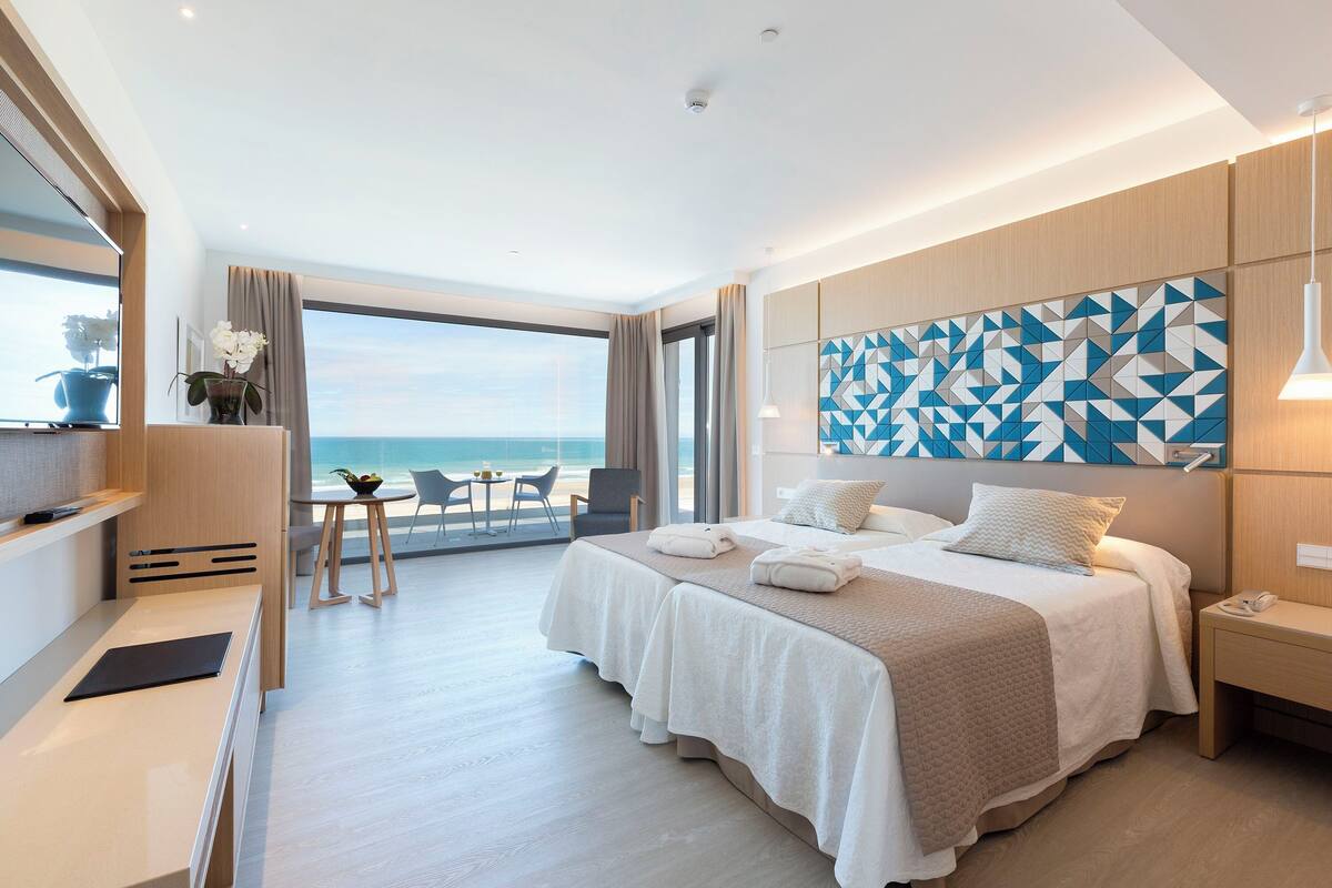 A modern hotel room with a large bed, a desk, and a view of the ocean.