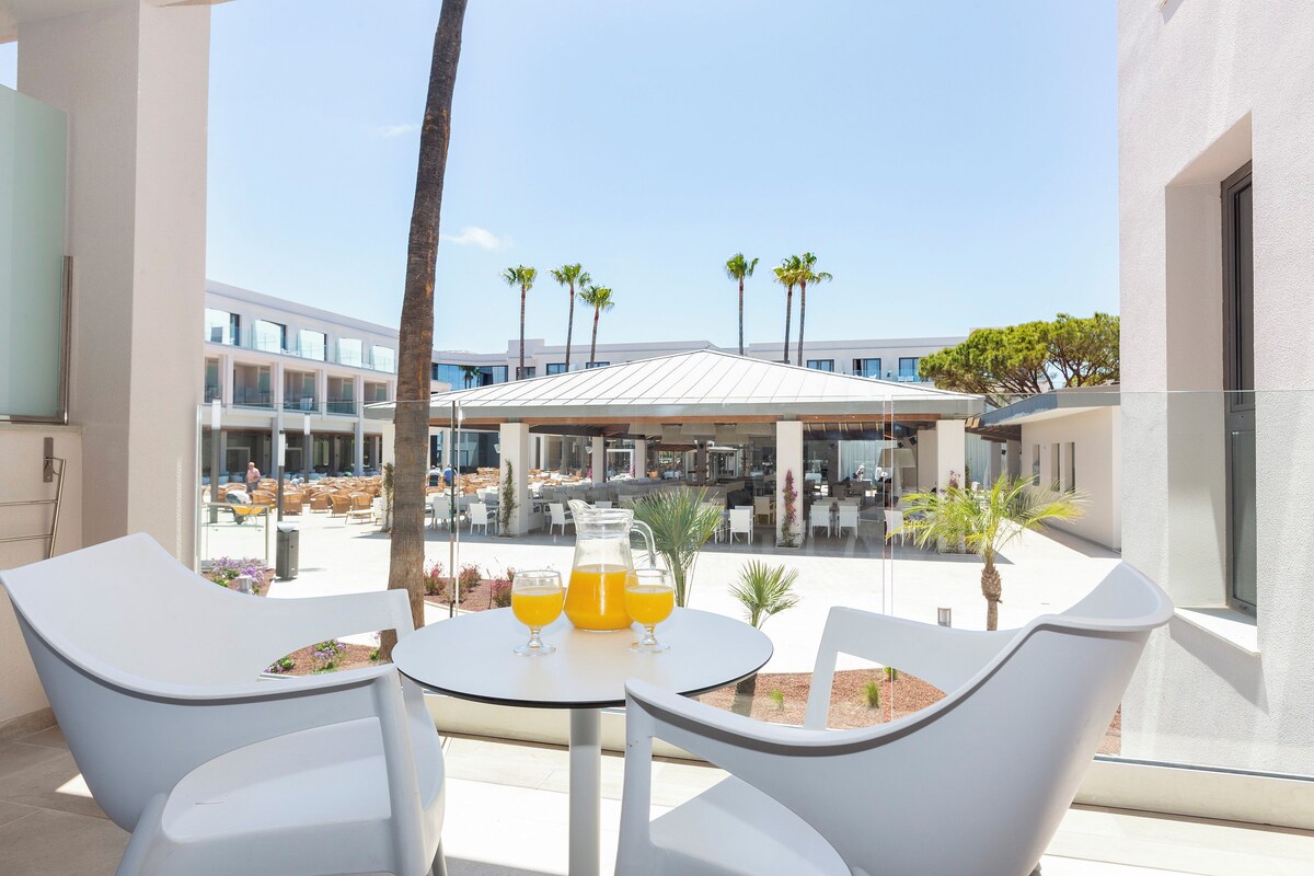 A balcony with two white chairs, a small table, and a pitcher of orange juice.
