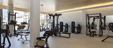 A spacious gym with various exercise equipment, including treadmills and weight machines, and large windows allowing natural light.