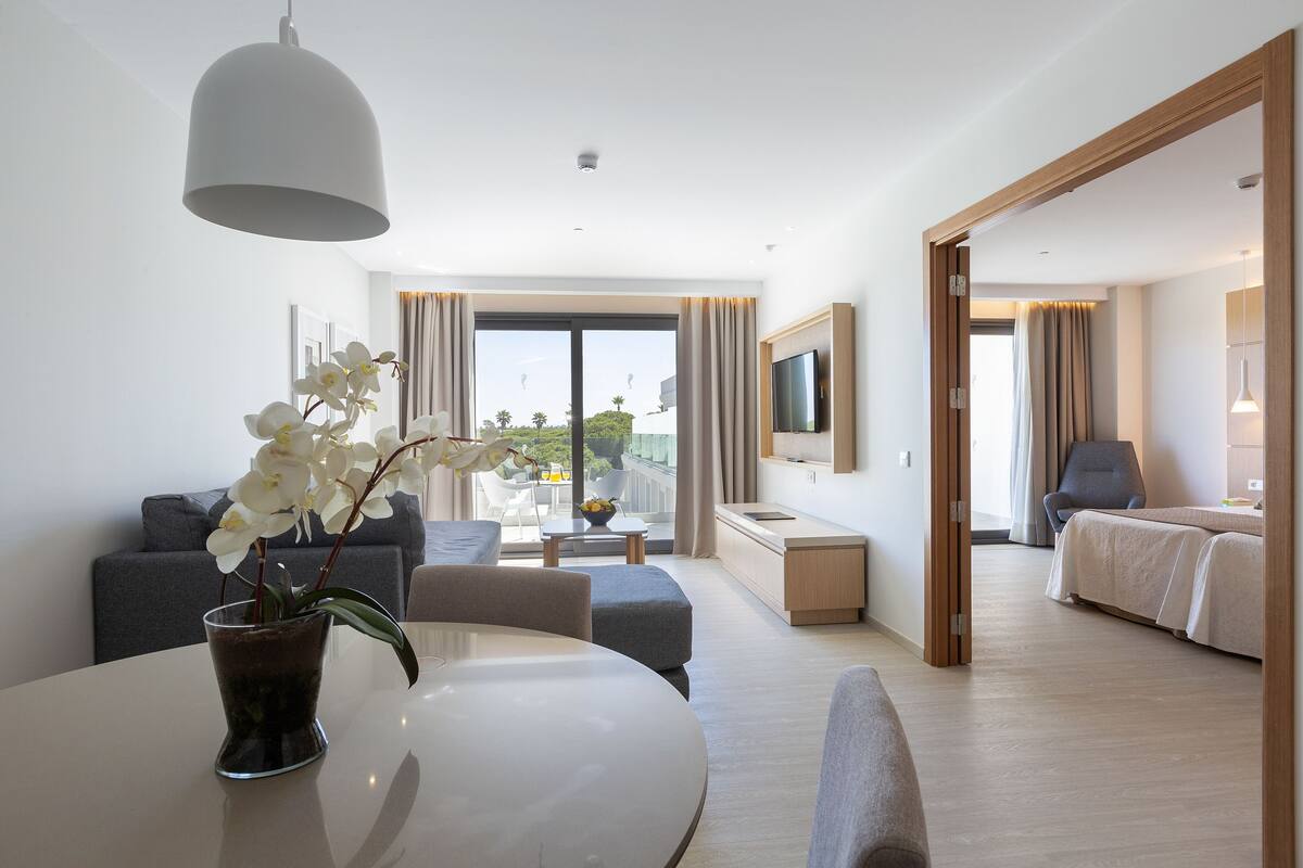 A modern hotel room with a dining area, sofa, and a bed.