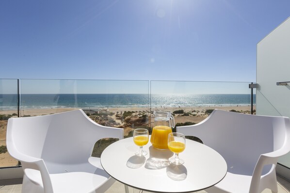 A table with two white chairs and a glass pitcher of orange juice, overlooking a beach.